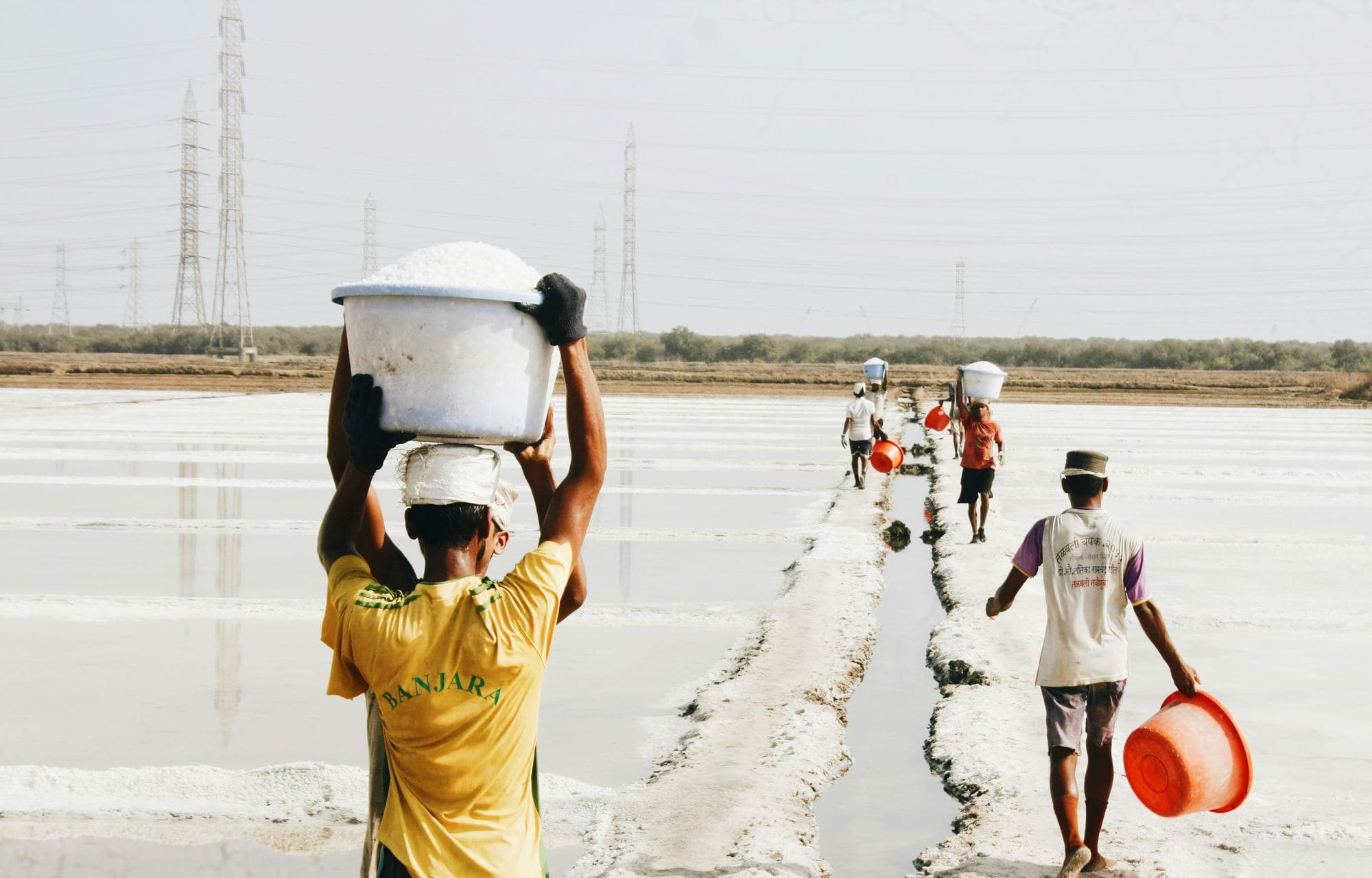 Workers carry loads along a salt pan